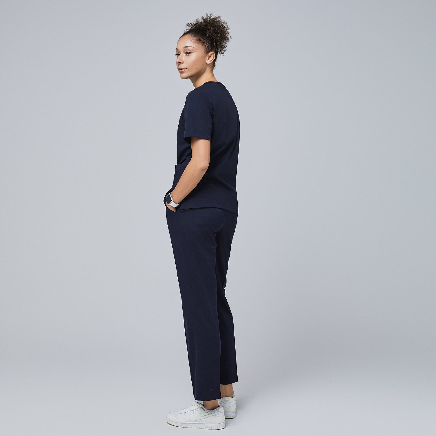 Image of Model wearing an eco navy scrub set, standing with hands in pockets, looking over shoulder,Eco Navy